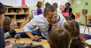 Obama looking through a magnifying glass at students.