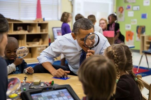 Obama looking through a magnifying glass at students.